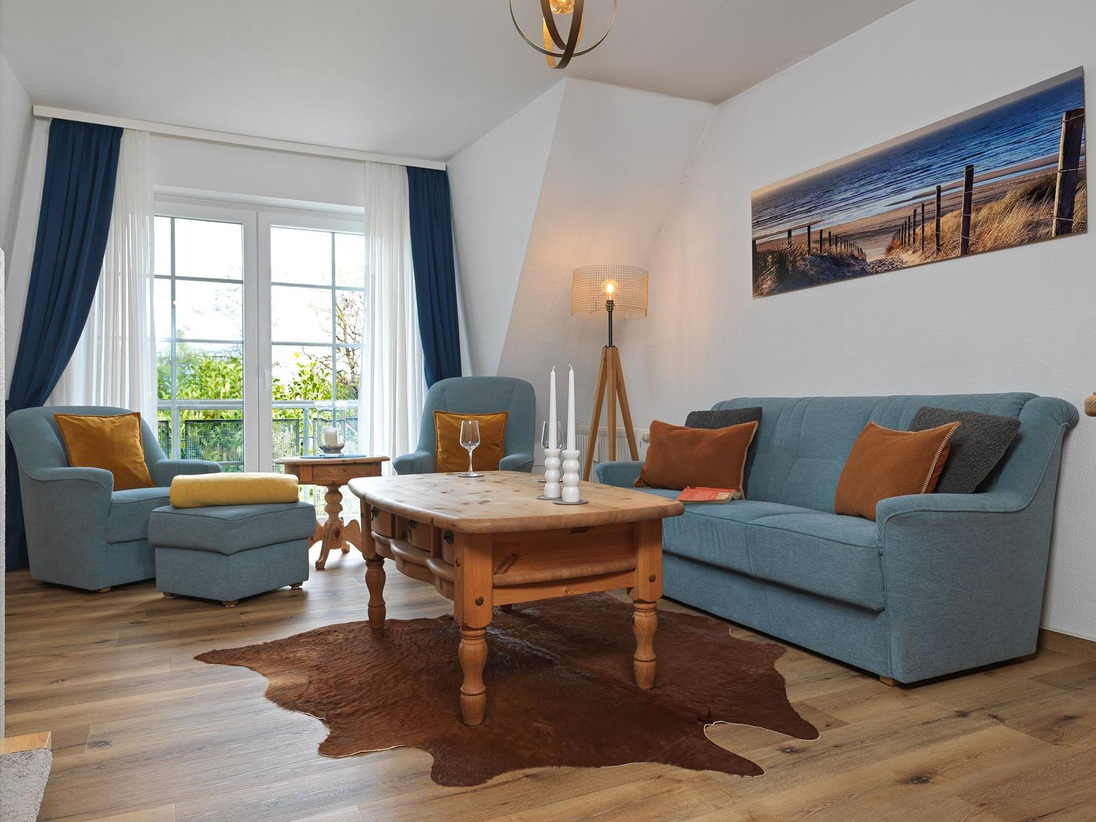 Wohnzimmer mit blauer Couch, Holztisch und Fenster zum Balkon.
