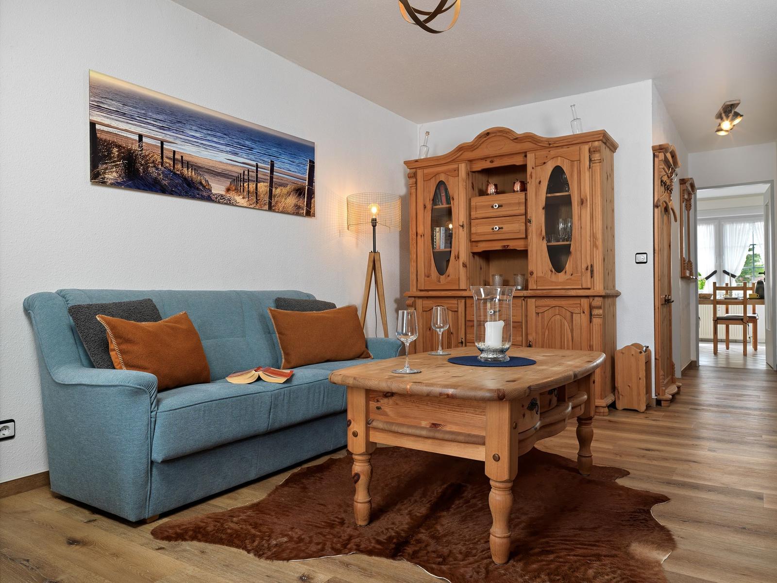 Ein Wohnzimmer mit Sofa, Holztisch und Schrank. Wandbild zeigt Strand.