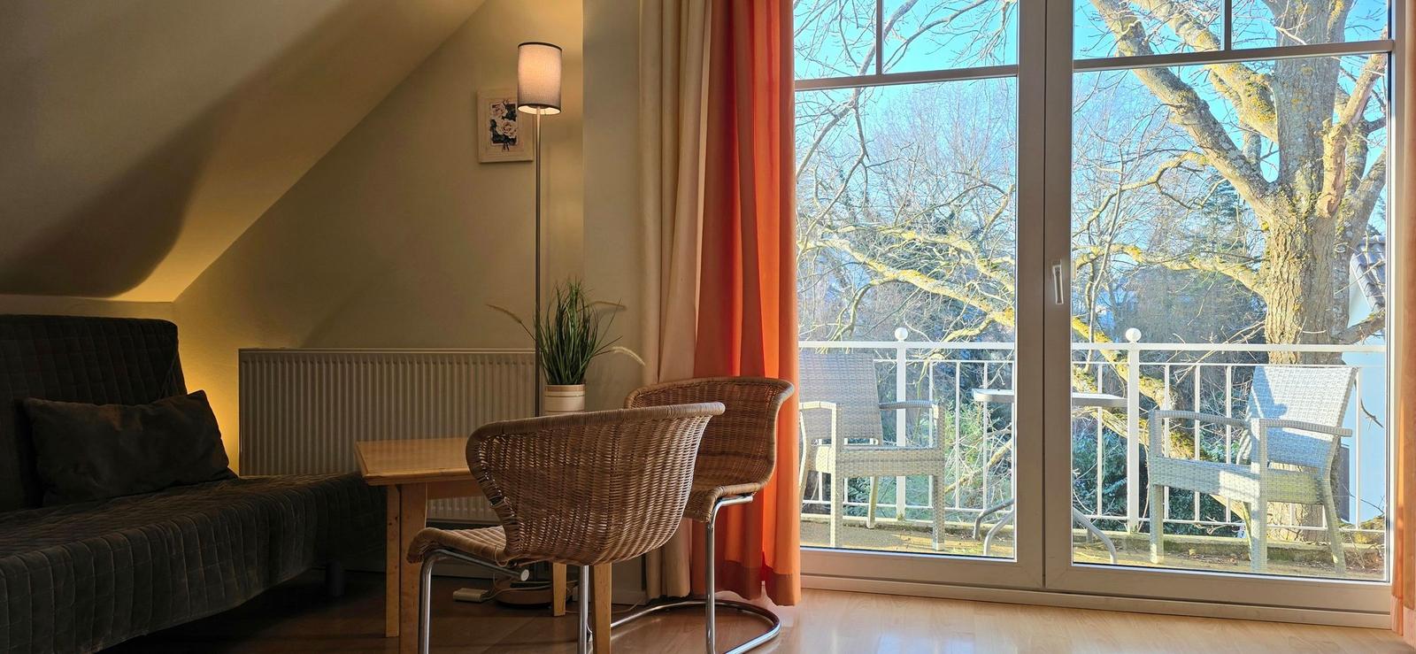 Wohnbereich mit Sitzgelegenheit und Balkonblick auf einen Baum.