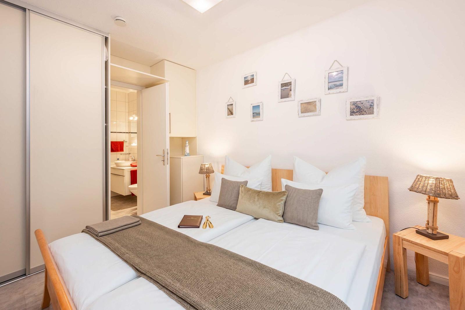 Schlafzimmer mit Doppelbett, Nachttischen und Bilder an der Wand. Badezimmer ist sichtbar.