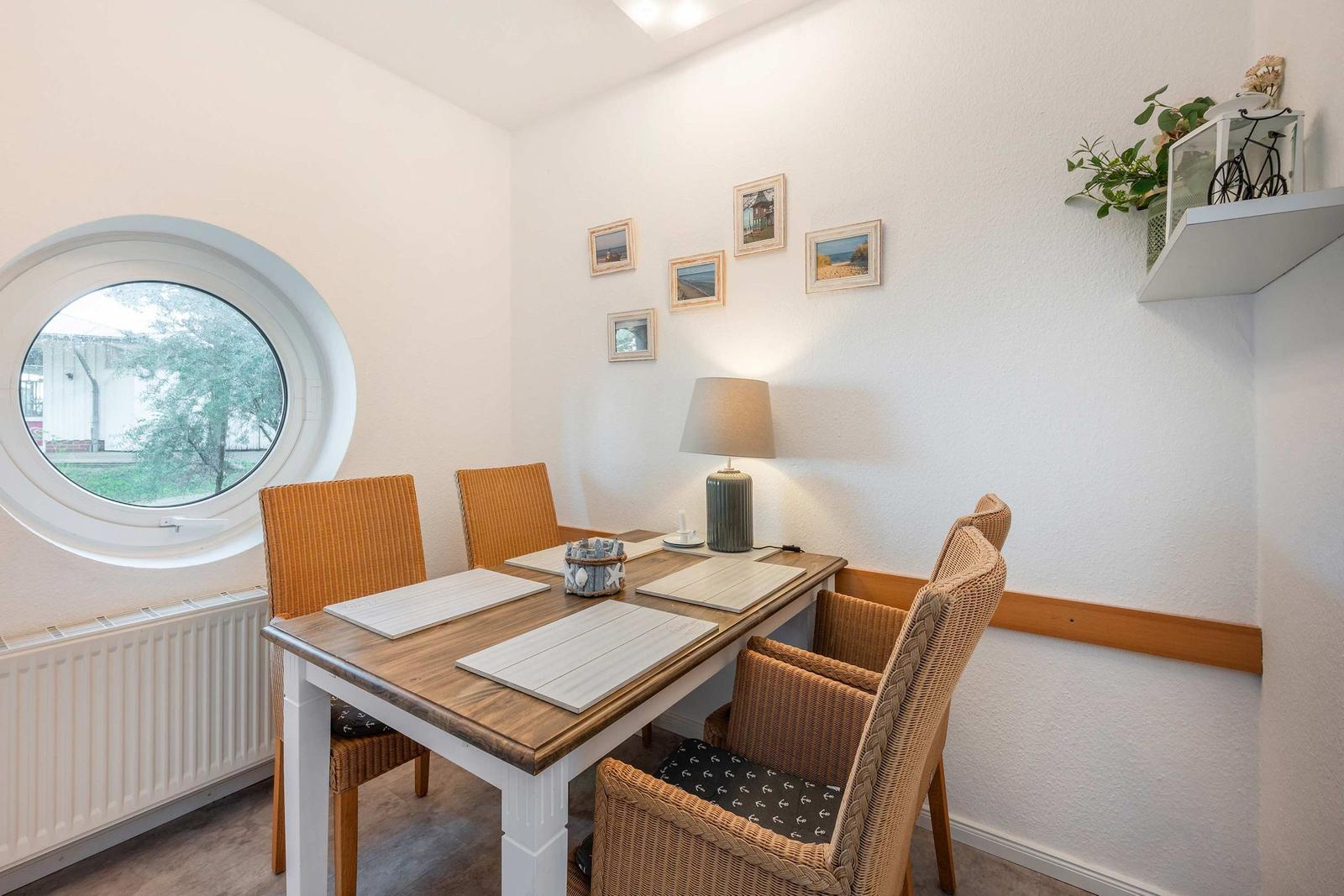Esszimmer mit runden Fenster, Tisch und Stühlen, Wandbilder und Lampe.