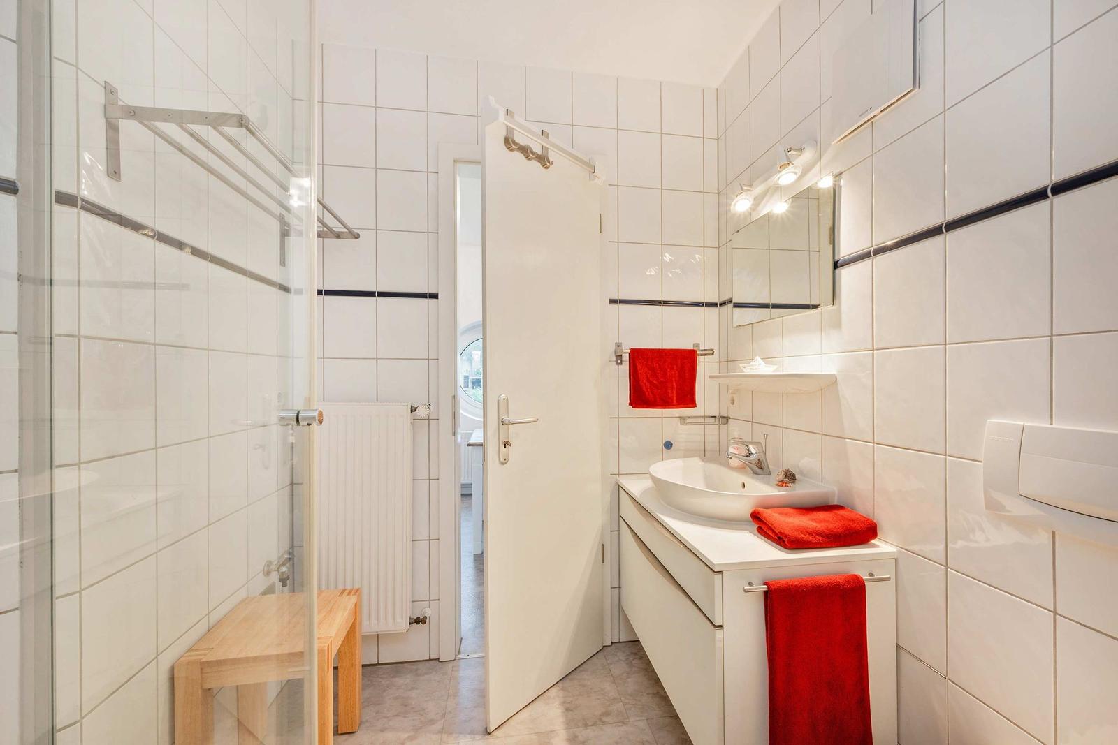 Badezimmer mit Dusche, Waschbecken und roten Handtüchern.