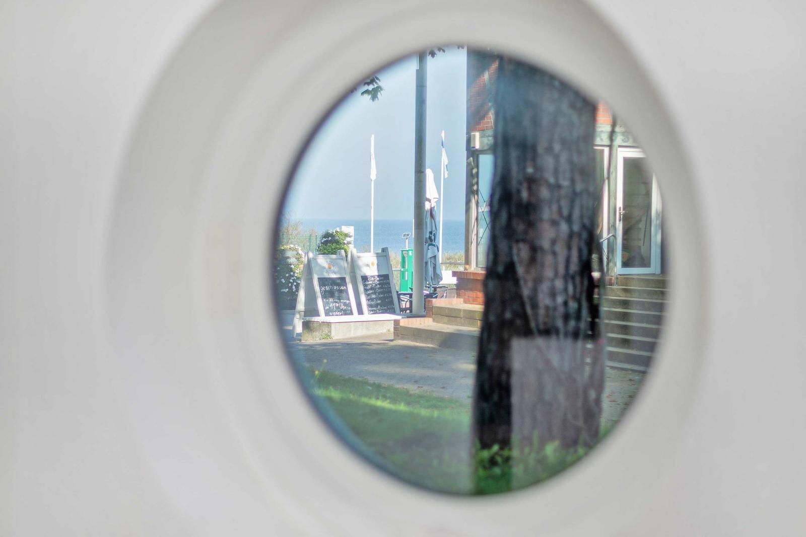 Durch runden Ausschnitt Blick auf Strand mit Tischen und Flaggen.