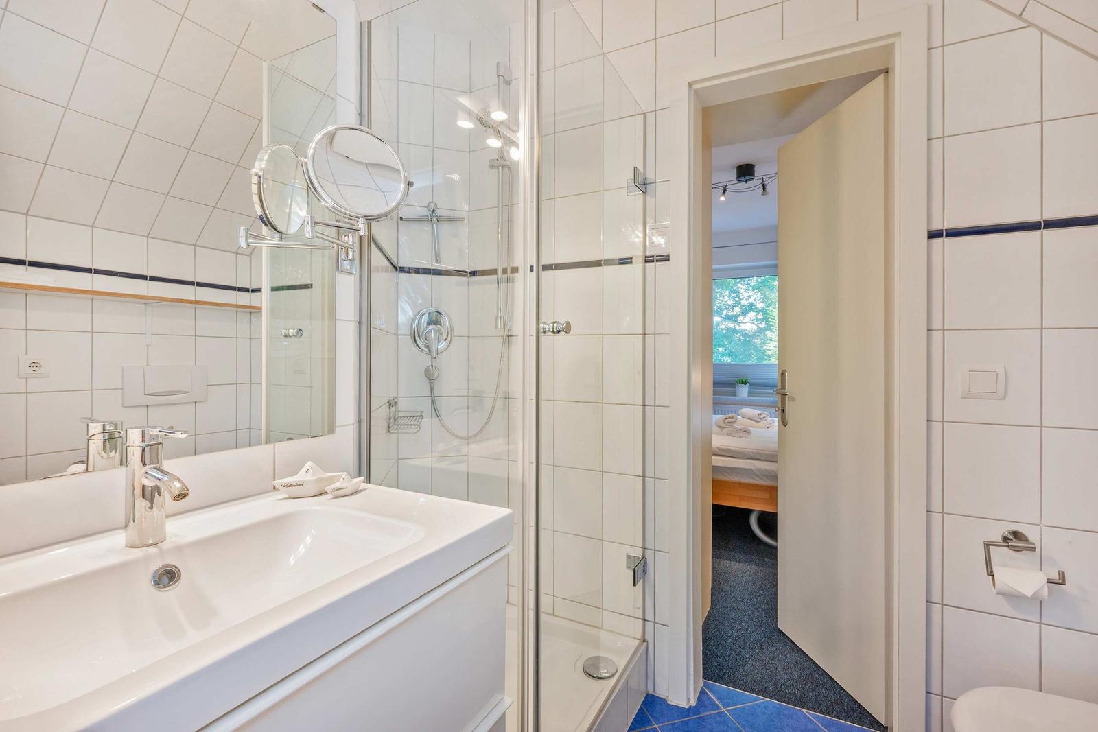 Badezimmer mit Dusche, Waschbecken und Blick in Schlafzimmer