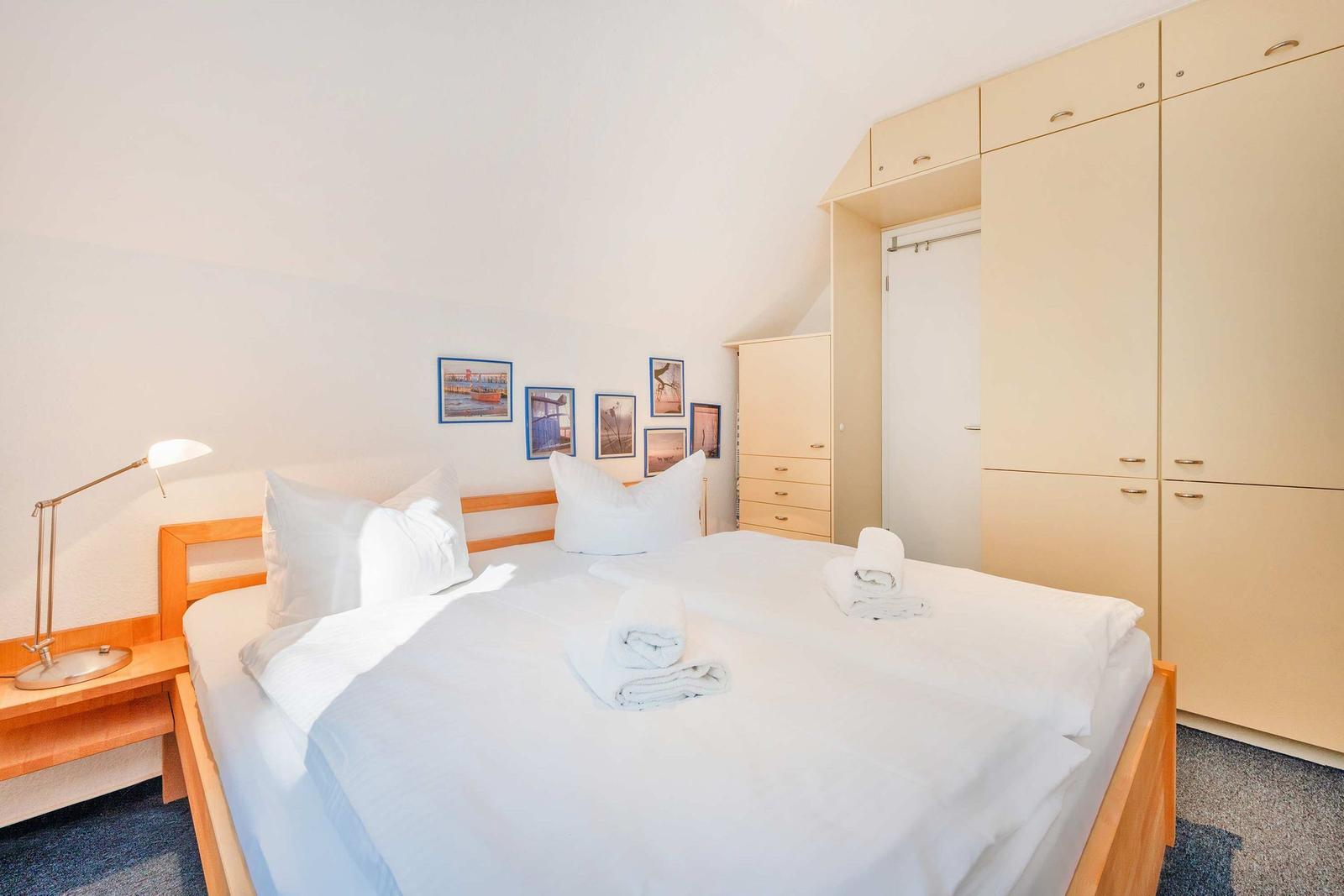 Schlafzimmer mit Doppelbett, Kleiderschrank und Wandbildern.