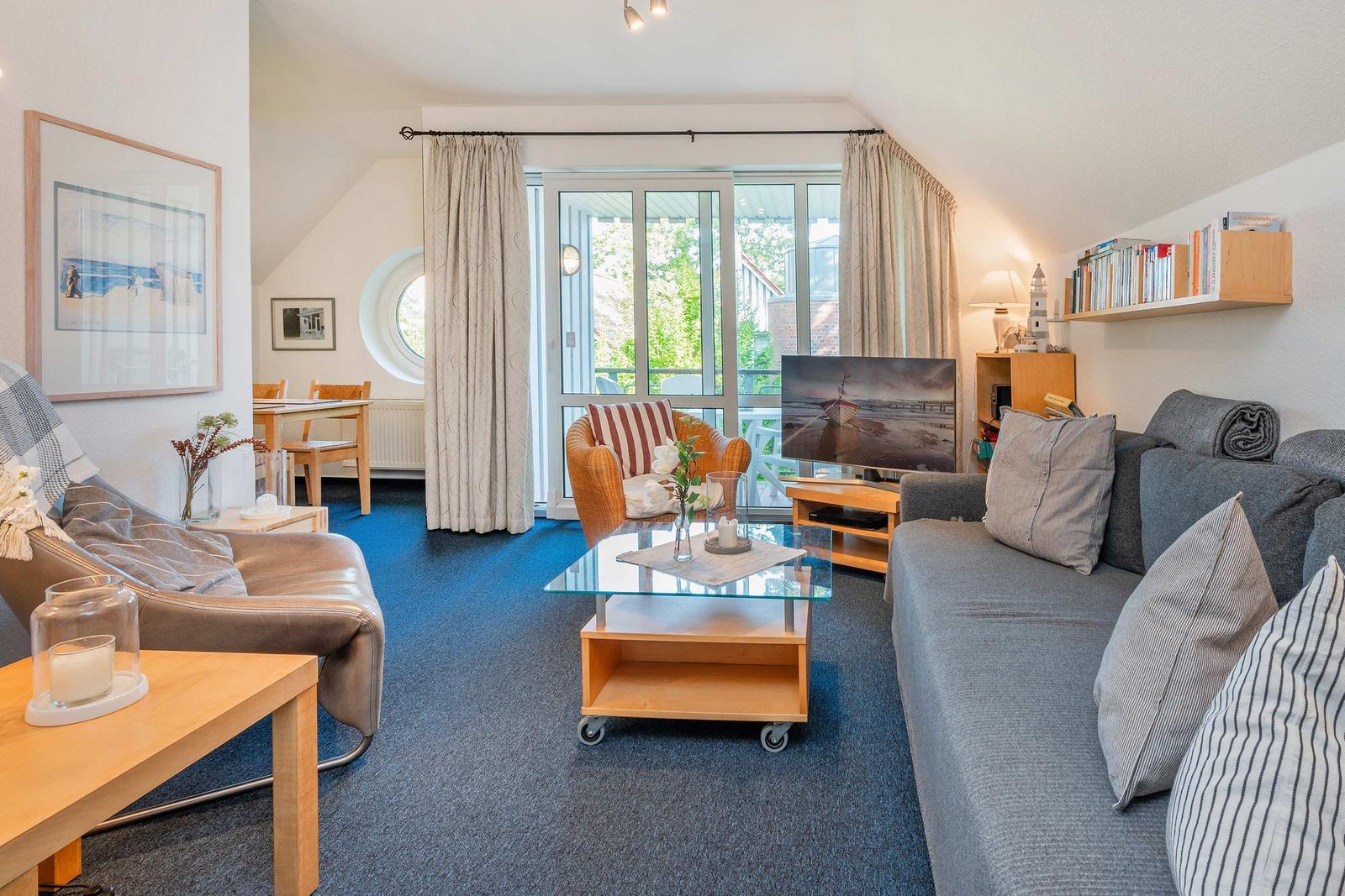 Wohnzimmer mit Sofa, Sessel und Glas-Tisch. Durchgang zu Balkon mit Blick.