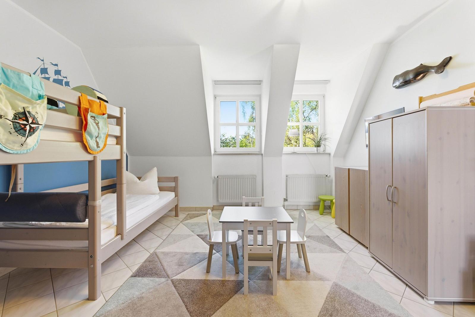 Ein Kinderzimmer mit Doppelstockbett, Tisch, Stühlen und Schränken unter einem Dach