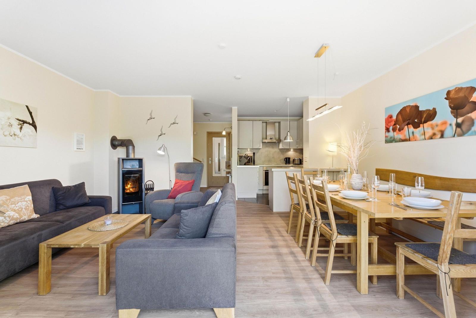 Wohn- und Essbereich mit Holztisch, Sofa und Kaminofen. Küche im Hintergrund.