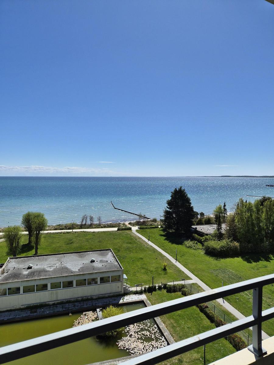 Blick vom Balkon auf Grünfläche, See und klaren Himmel.