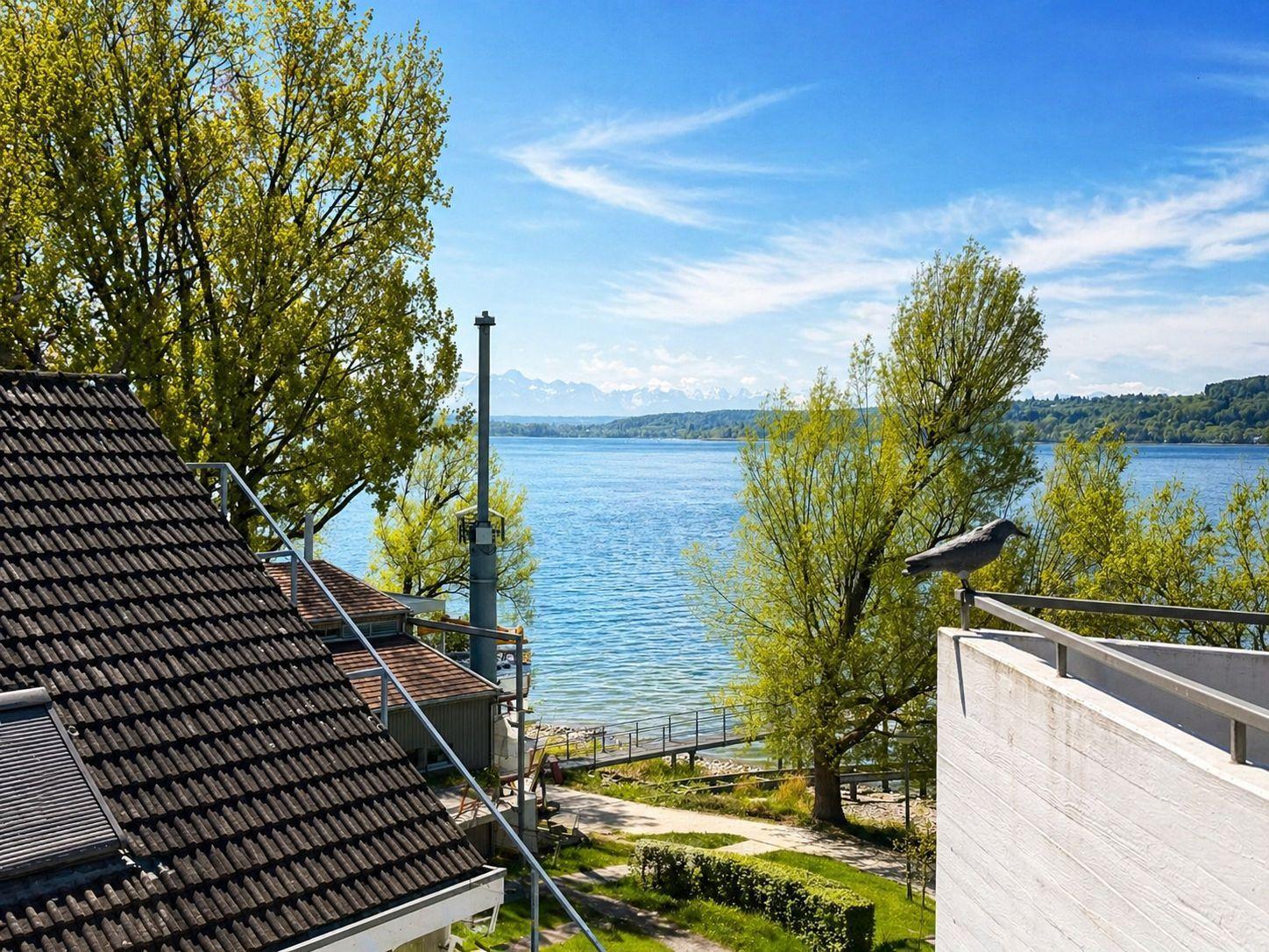 Blick auf einen See mit Bäumen und einem Vogel auf einem Geländer.