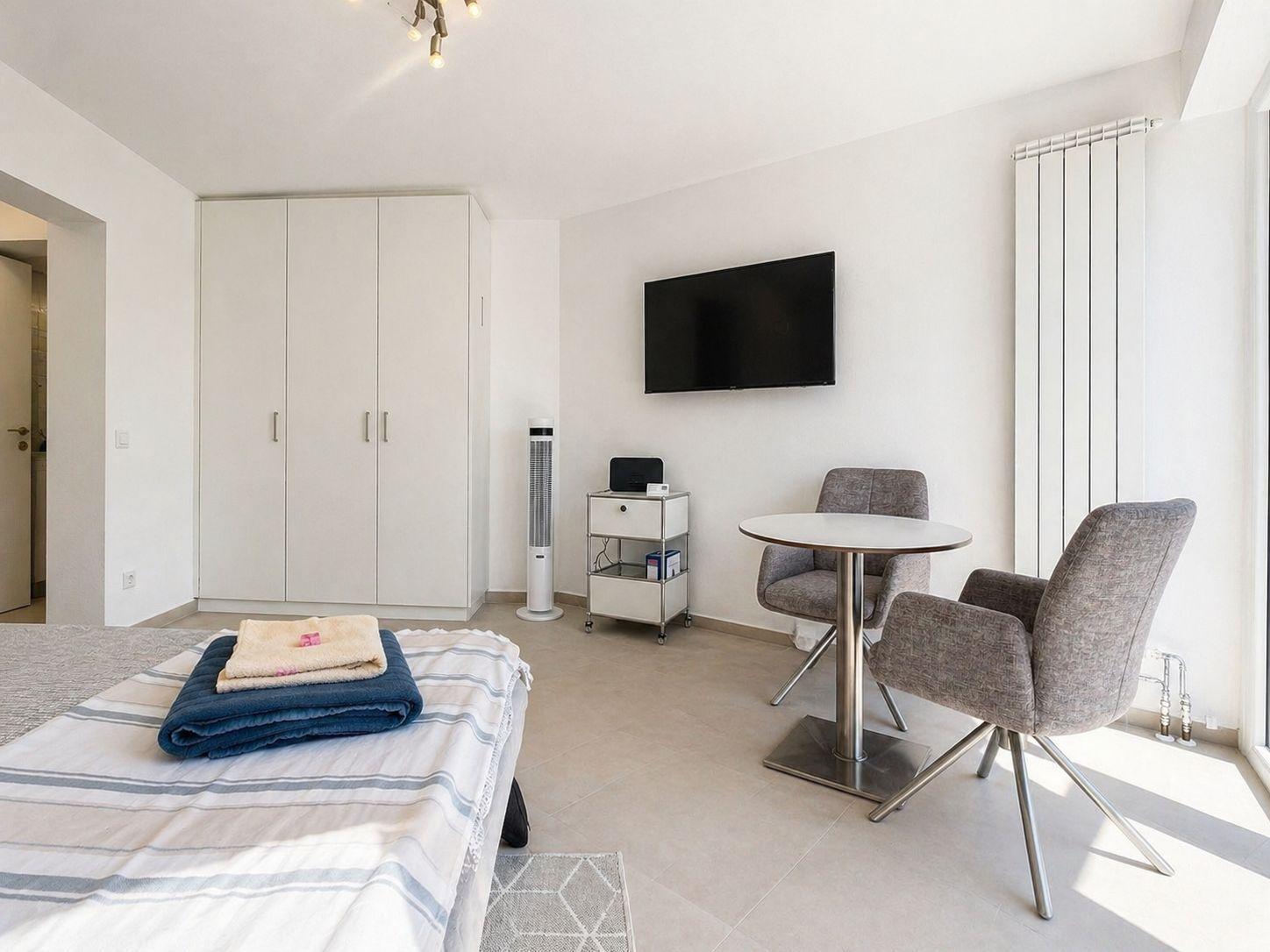 Schlafzimmer mit Bett, Kleiderschrank, Fernseher und Sitzgruppe.