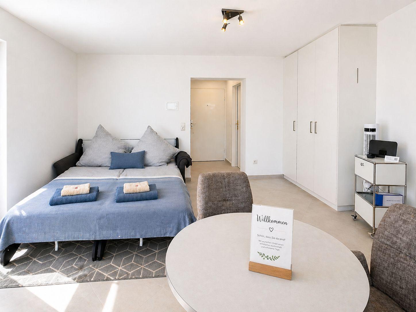Schlafzimmer mit Bett, Schrank und runden Tisch. Willkommen-Schild auf Tisch.