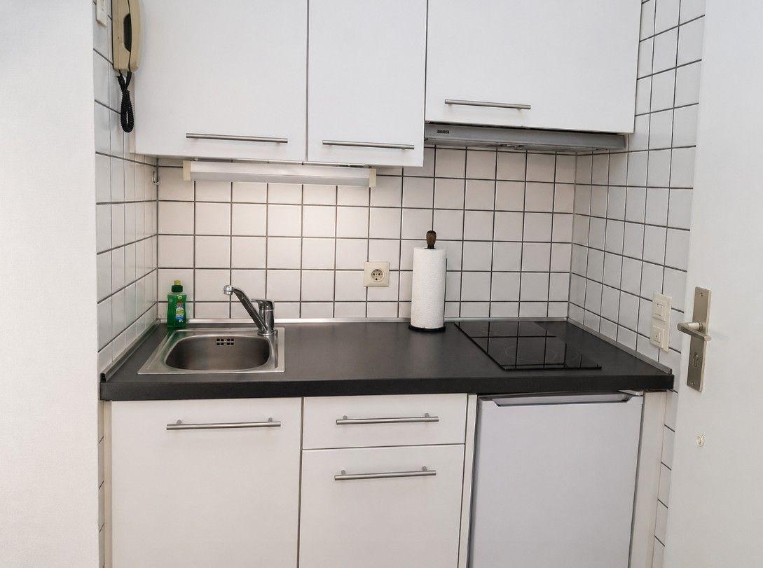 Küche mit weißen Schränken, schwarzer Arbeitsplatte, Spüle und Induktionskochfeld.