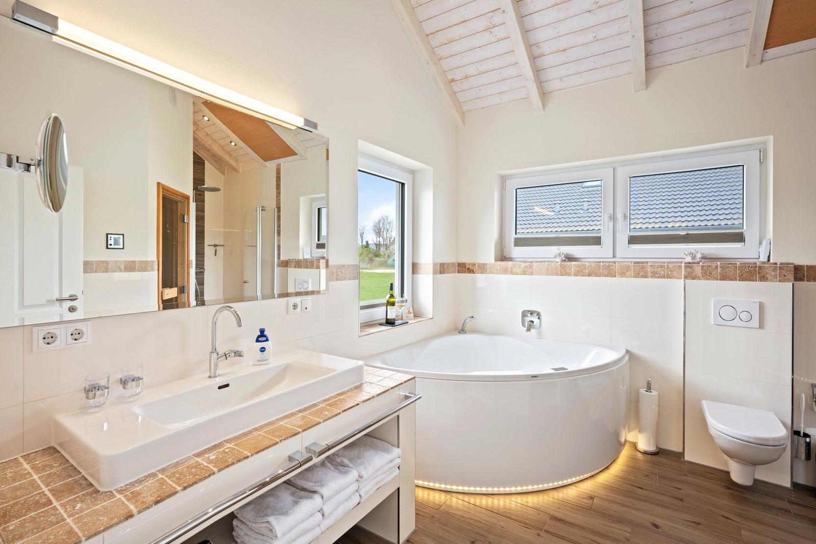 Badezimmer mit Badewanne, Waschbecken und Toilette. Holzdecke und Fenster mit Blick.