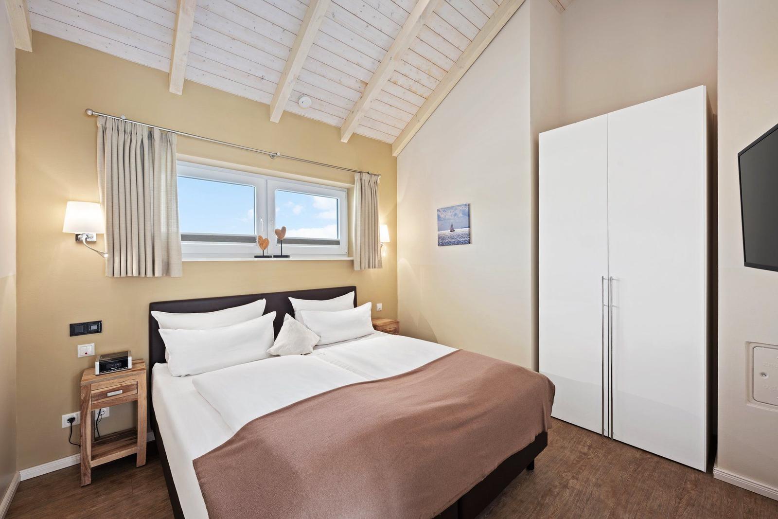 Schlafzimmer mit Doppelbett, Fenster, Kleiderschrank und Wandbild.