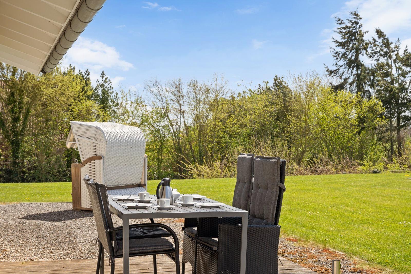Terrasse mit Tisch, Stühlen und Gartenblick. Hintergrund: grüner Rasen und Bäume.