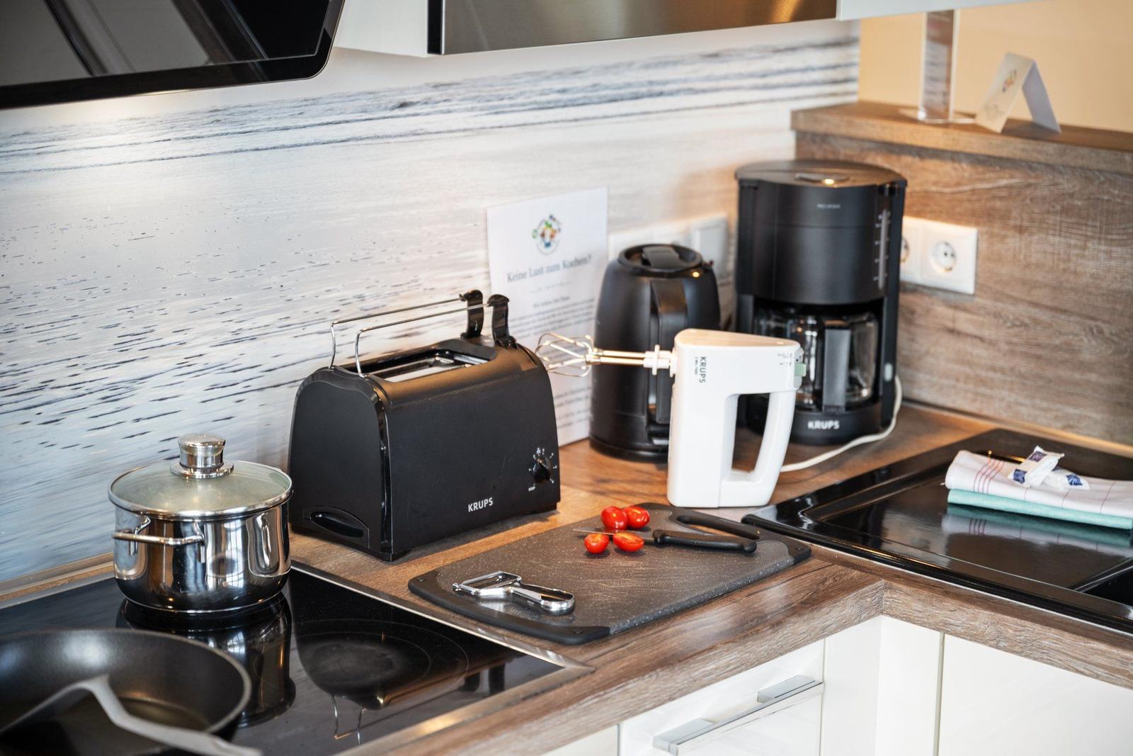Küchenzeile mit Toaster, Kaffeemaschine und Kochutensilien auf Arbeitsfläche.