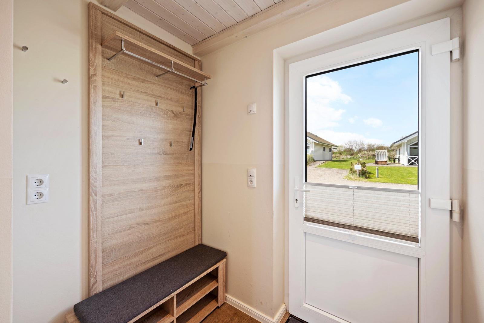 Eingangsbereich mit Holzgarderobe, Sitzbank und Fenster zum Garten.