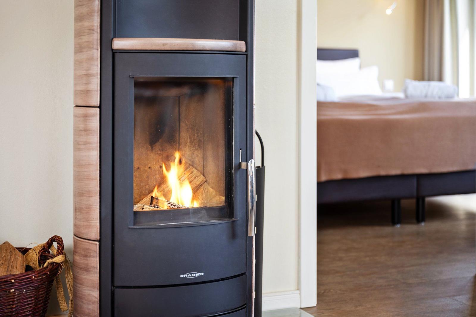 Kaminofen mit brennendem Holz. Im Hintergrund ist ein Bett sichtbar.