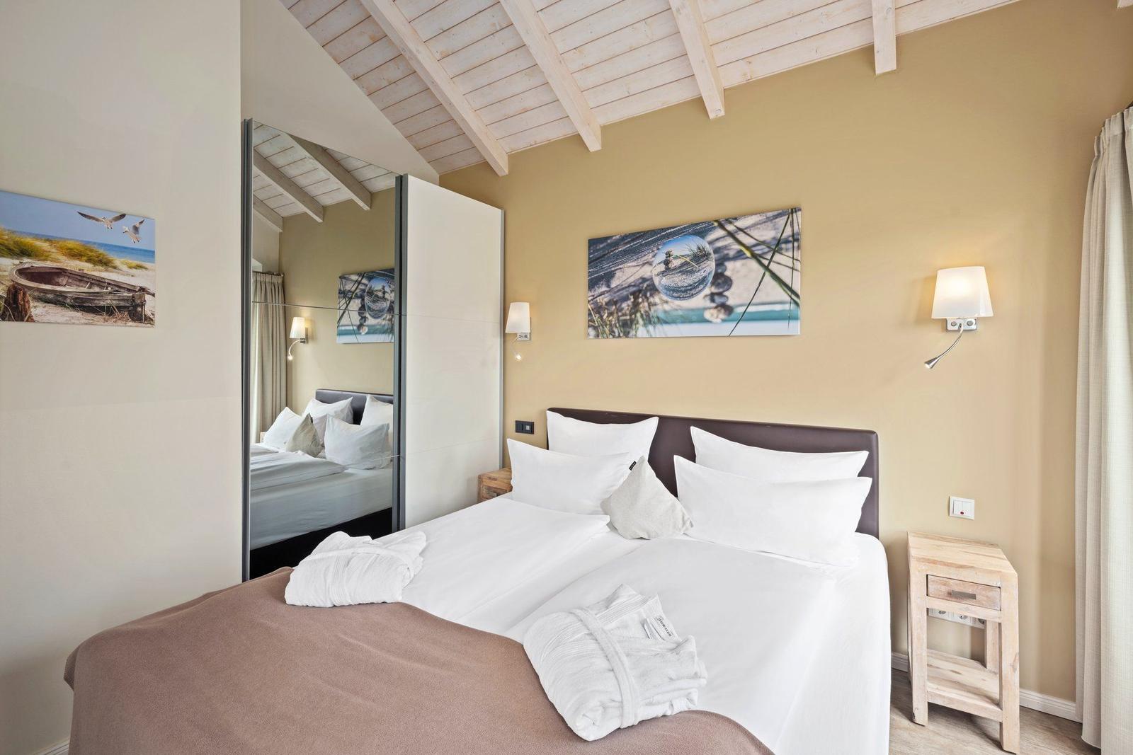 Schlafzimmer mit Doppelbett, Wandbildern und Holzdecke.