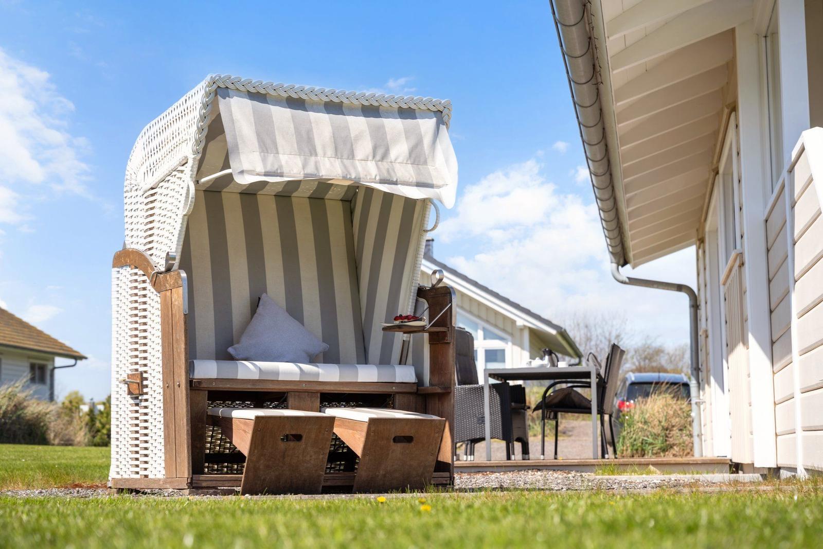 Ein Strandkorb mit Streifenbezug steht auf dem Gras vor einem Haus.