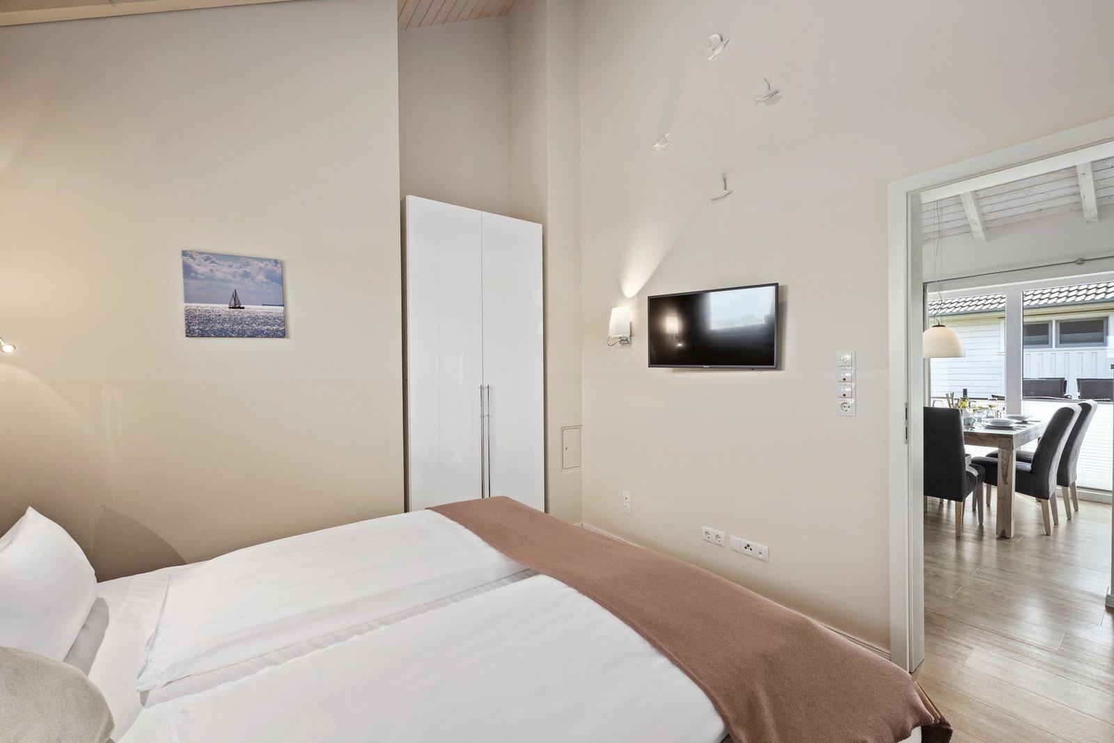 Schlafzimmer mit Bett, Kleiderschrank und TV. Durchgang zur Essnische mit Tisch und Stühlen.
