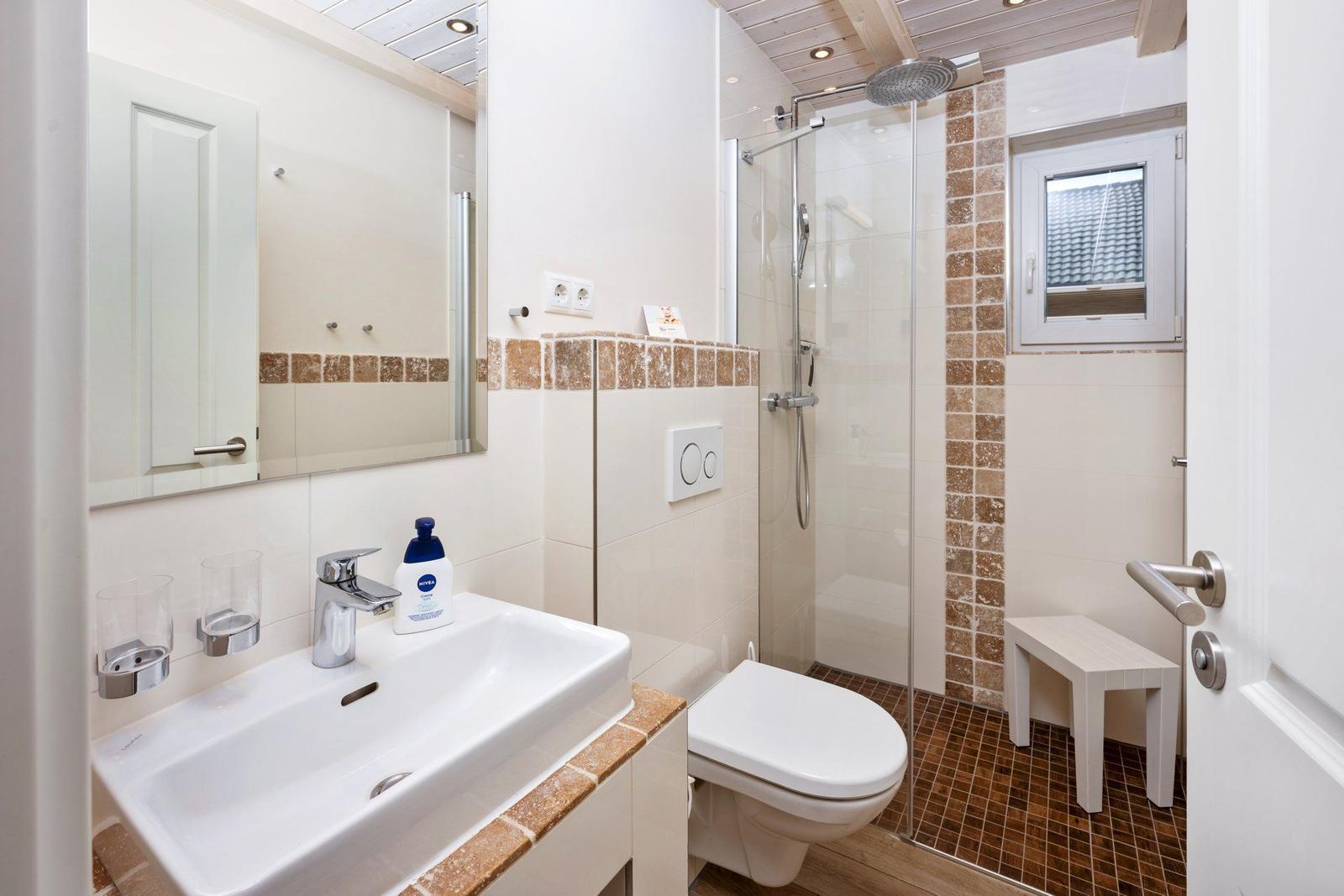 Badezimmer mit Dusche, Waschbecken und Toilette. Holzdecke und Fliesen.