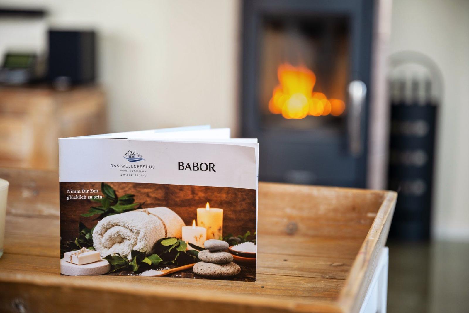 Ein Wellnessmagazin liegt auf einem Holztisch vor einem brennenden Kamin.
