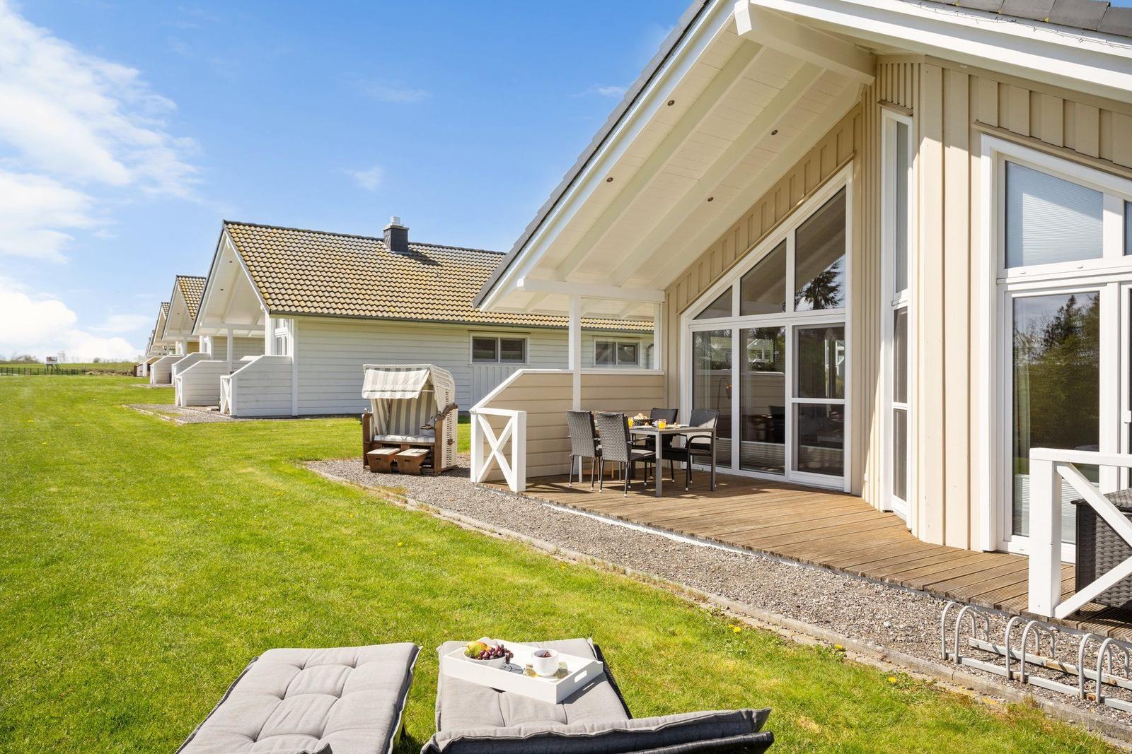 Terrasse mit Tisch und Stühlen, Gartenliegen und Strandkorb vor einem Ferienhaus.