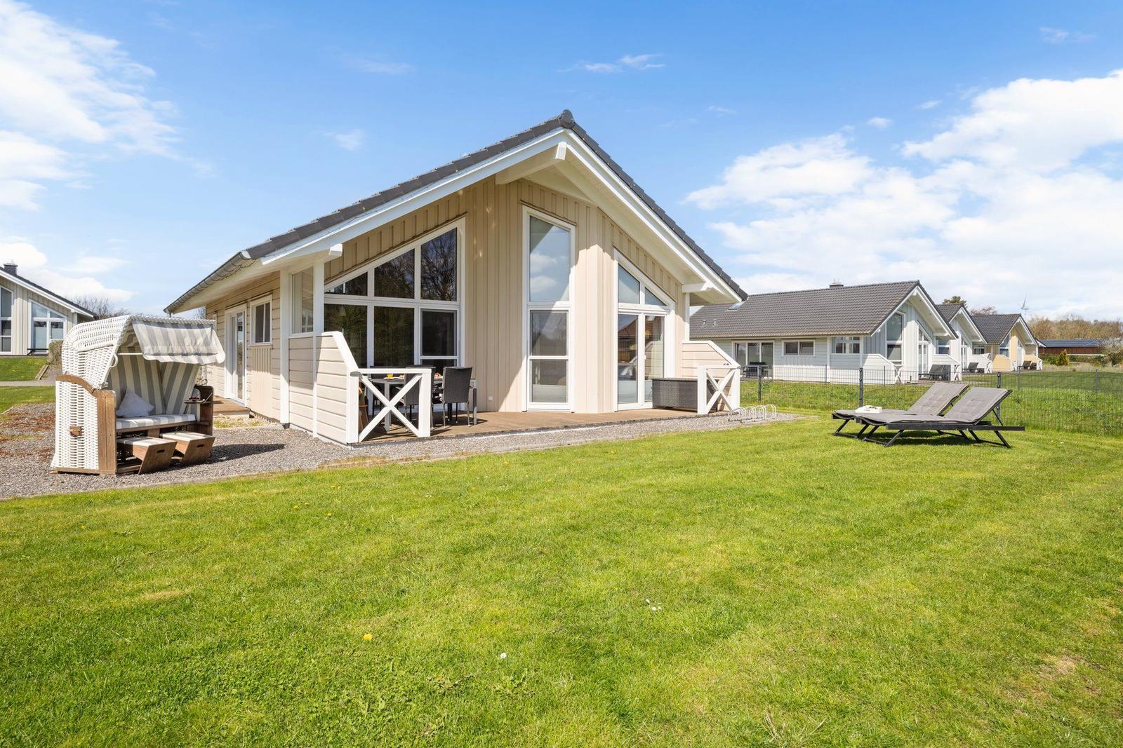 Modernes Ferienhaus mit Terrasse, Garten und Strandkorb. Hintergrund: weitere Häuser.