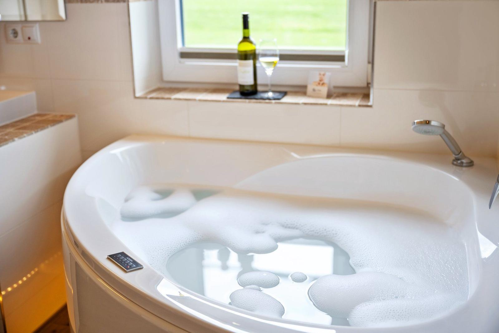 Eine Badewanne mit Schaum, daneben steht eine Flasche und ein Glas.