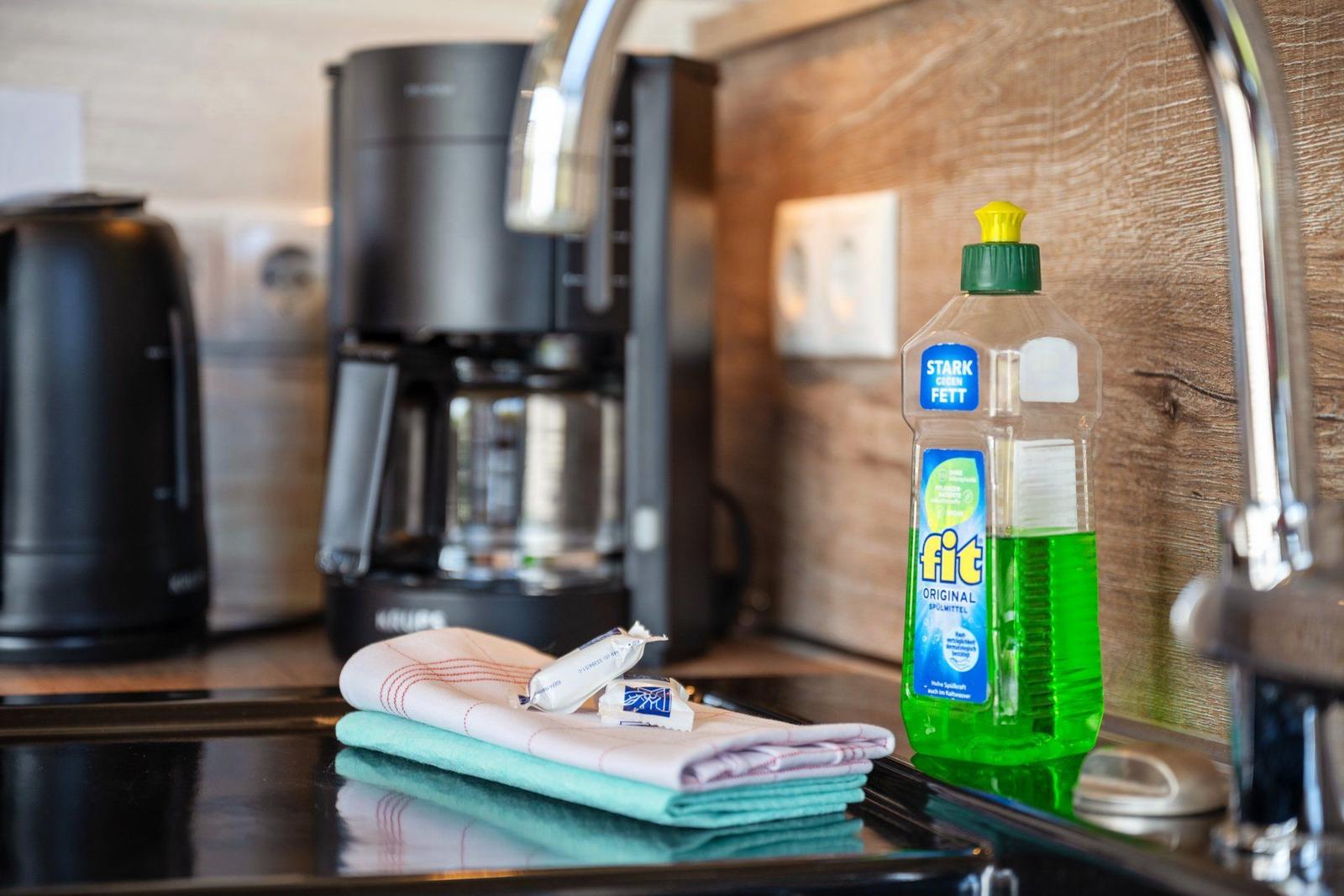 Küchenzeile mit Kaffeemaschine, Spülmittel und Handtuch auf Arbeitsfläche.