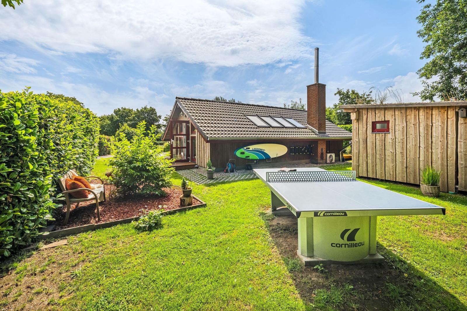 Hinterhof mit Tischtennisplatte, Gartenhaus und Holzhaus unter blauem Himmel.