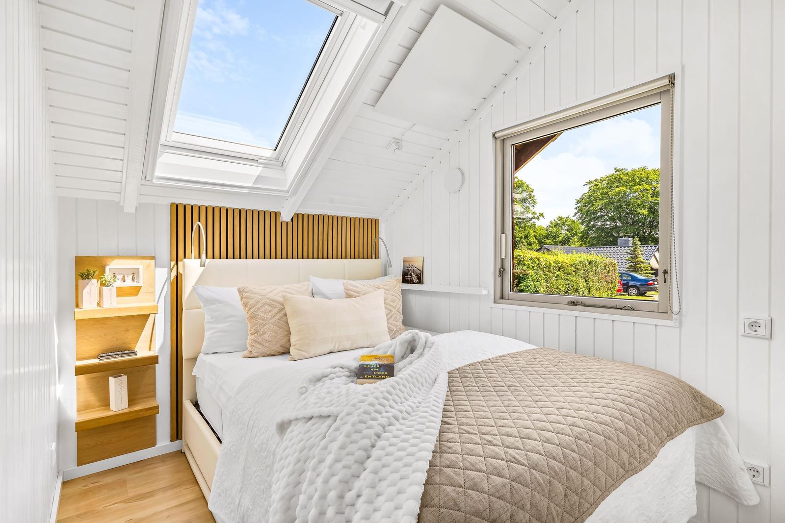 Schlafzimmer mit Dachfenster und Fenster zum Garten. Bett mit Kissen und Decke.