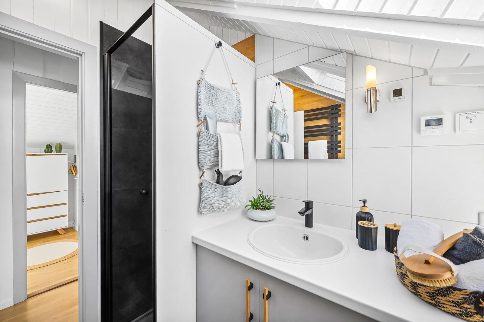Badezimmer mit Dusche, Waschbecken und Spiegel. Weiße Wände und Holzboden.