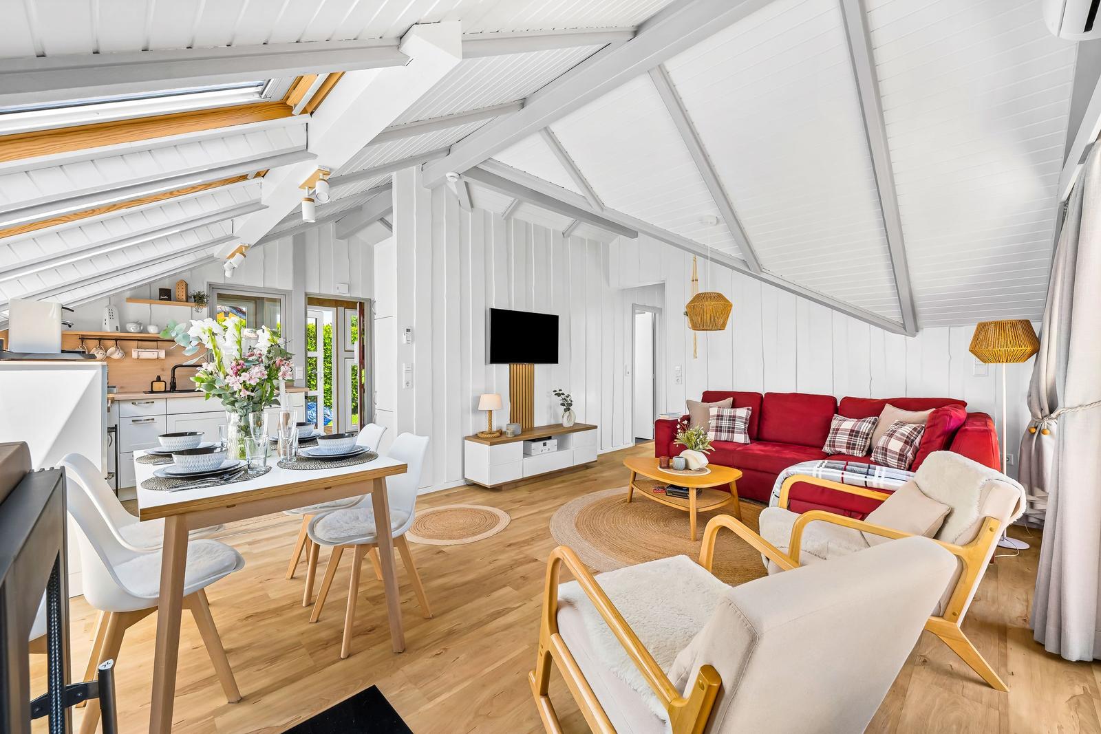 Wohn- und Essbereich mit rotem Sofa, Esstisch und Holzboden unter hohem Dach