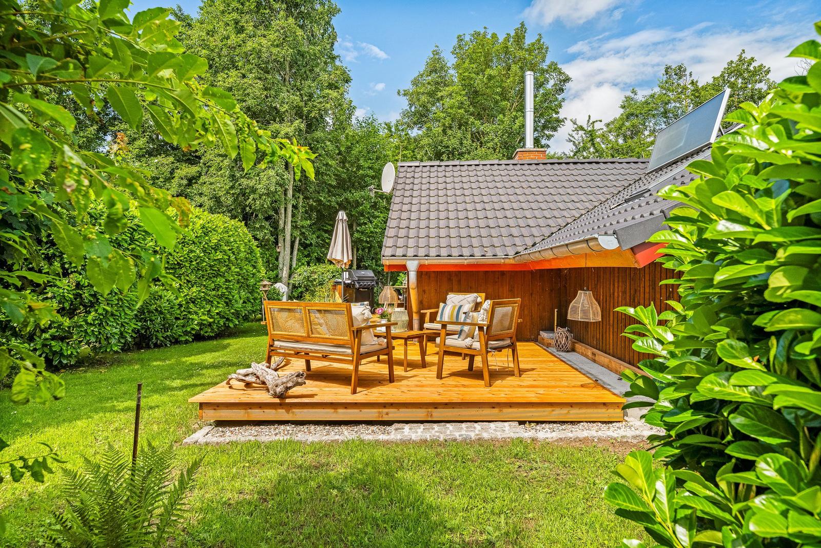 Terrasse mit Holzmöbeln, Grill und Garten. Haus mit Solaranlage und Dachgasträume.