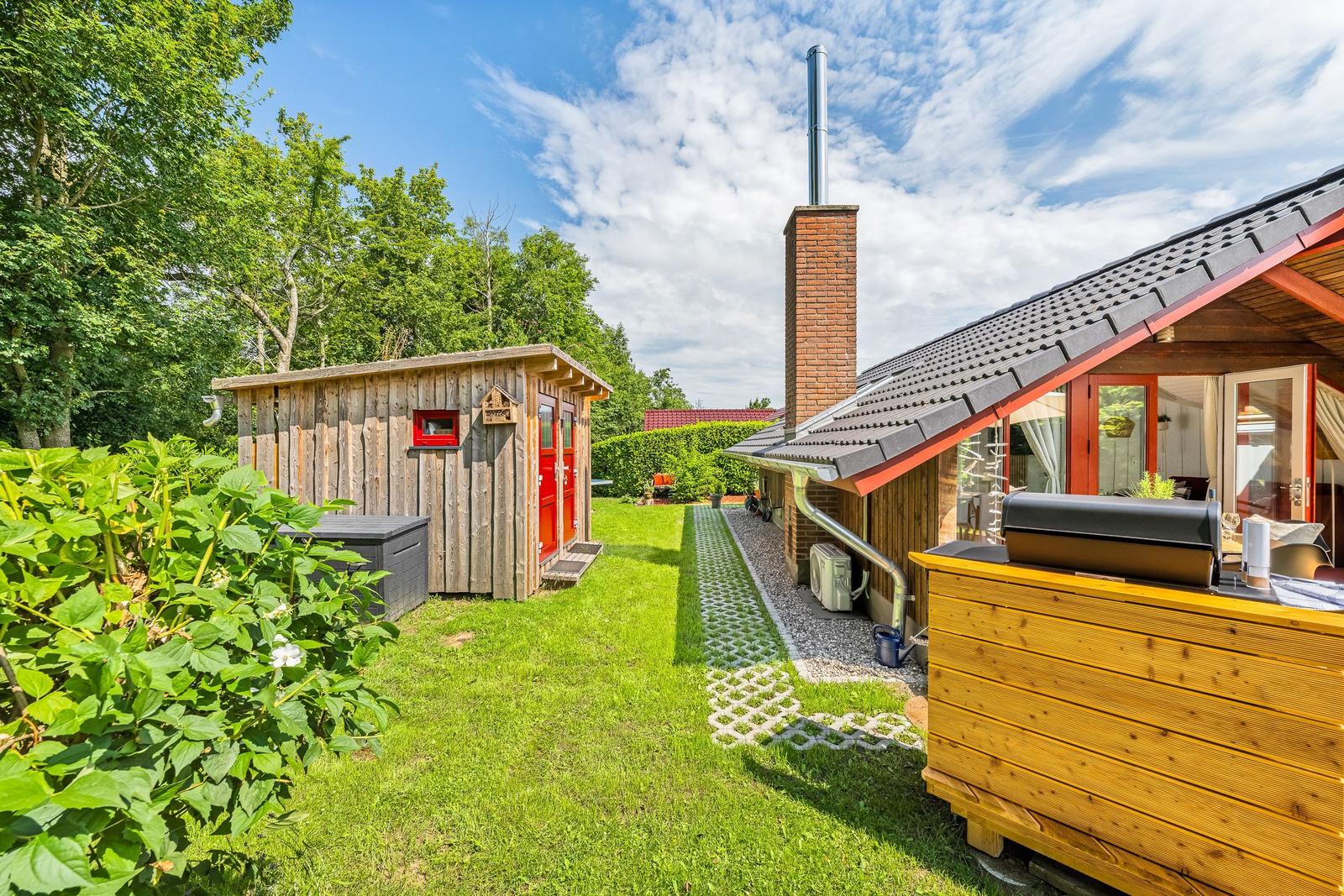 Haus mit Grillplatz, Holzschuppen und grünem Garten unter blauem Himmel.