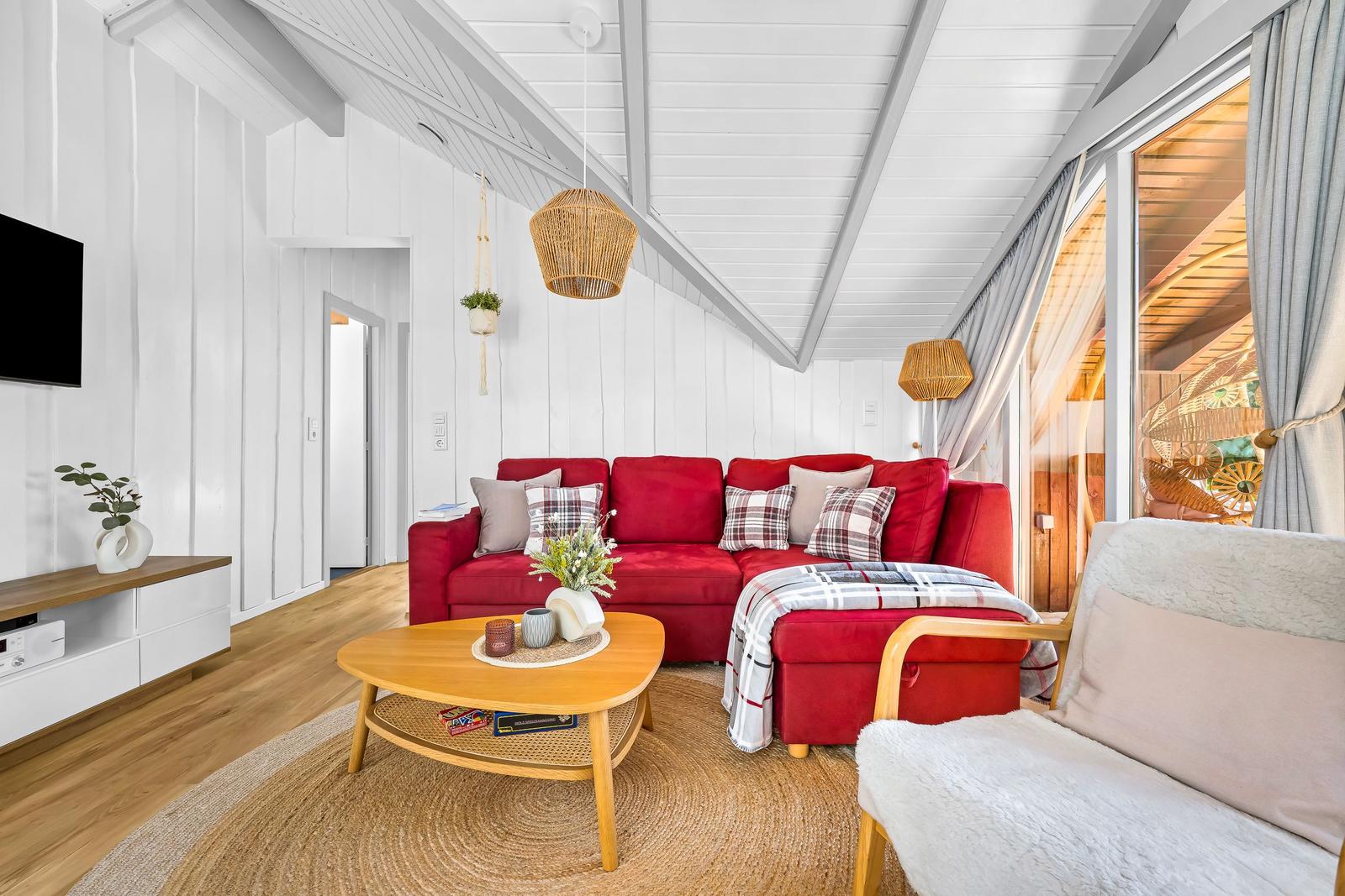 Ein Wohnzimmer mit rotem Sofa, Holztisch und weißen Wänden.
