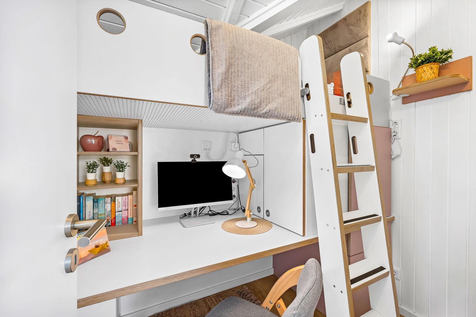 Hochbett mit Arbeitsplatz und Schreibtisch. Bücherregal, Monitor und Lampe sind vorhanden.