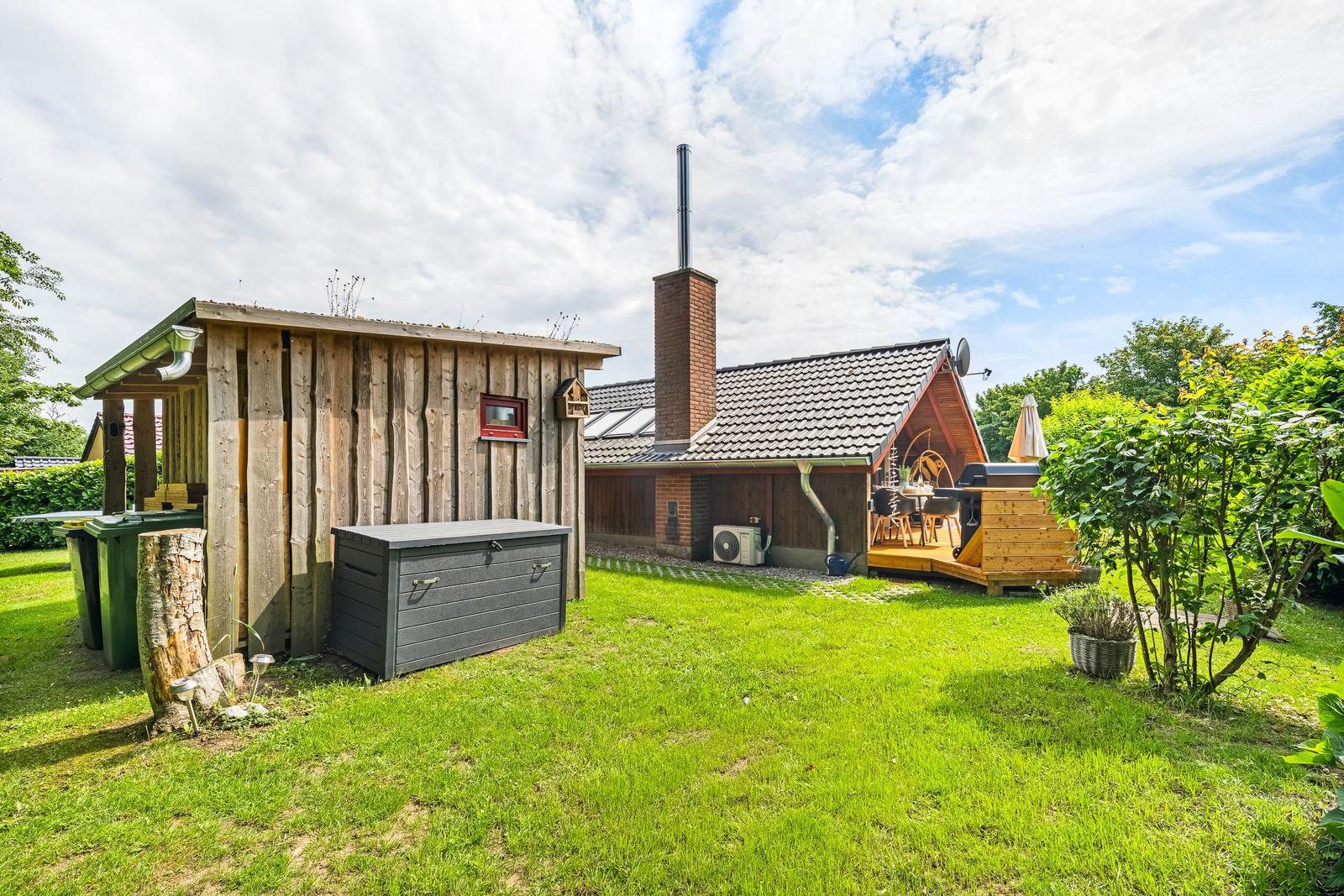 Haus mit Holzschuppen, Grillplatz und Garten. Rauchfang und Terrasse sind sichtbar.