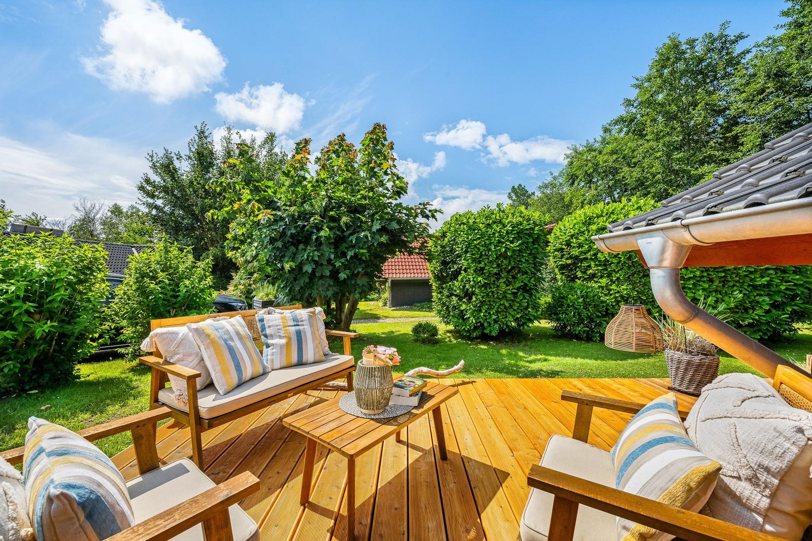 Holzterrasse mit Sitzgelegenheiten und Blick auf grünen Garten.