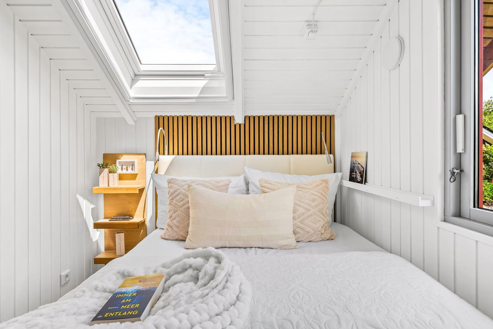 Schlafzimmer mit Dachfenster, Holz-Kopfteil und Bücherregal an der Wand.