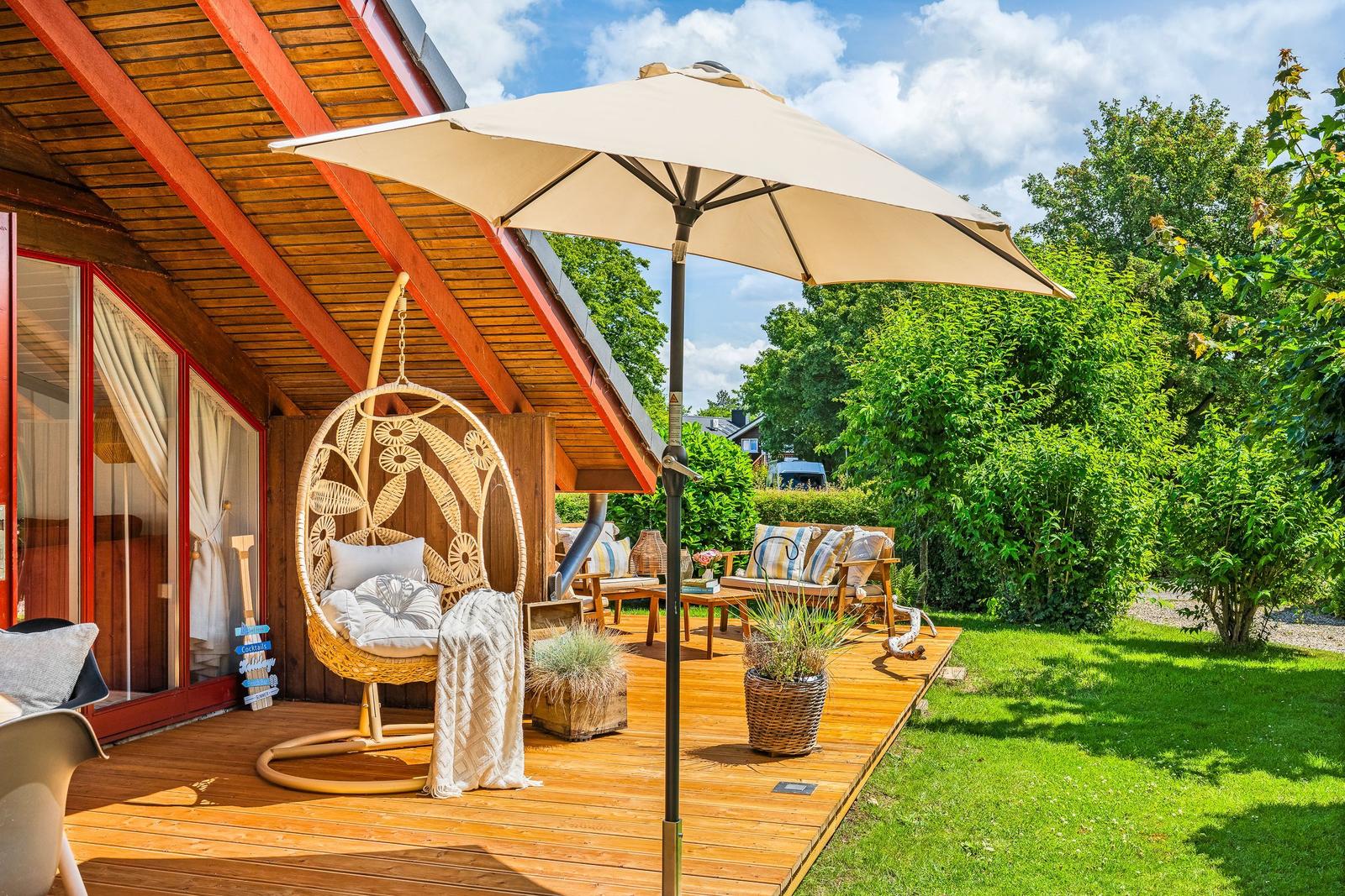 Terrasse mit Hängesessel, Sonnenschirm und Gartenmöbeln unter einem Holzdach.