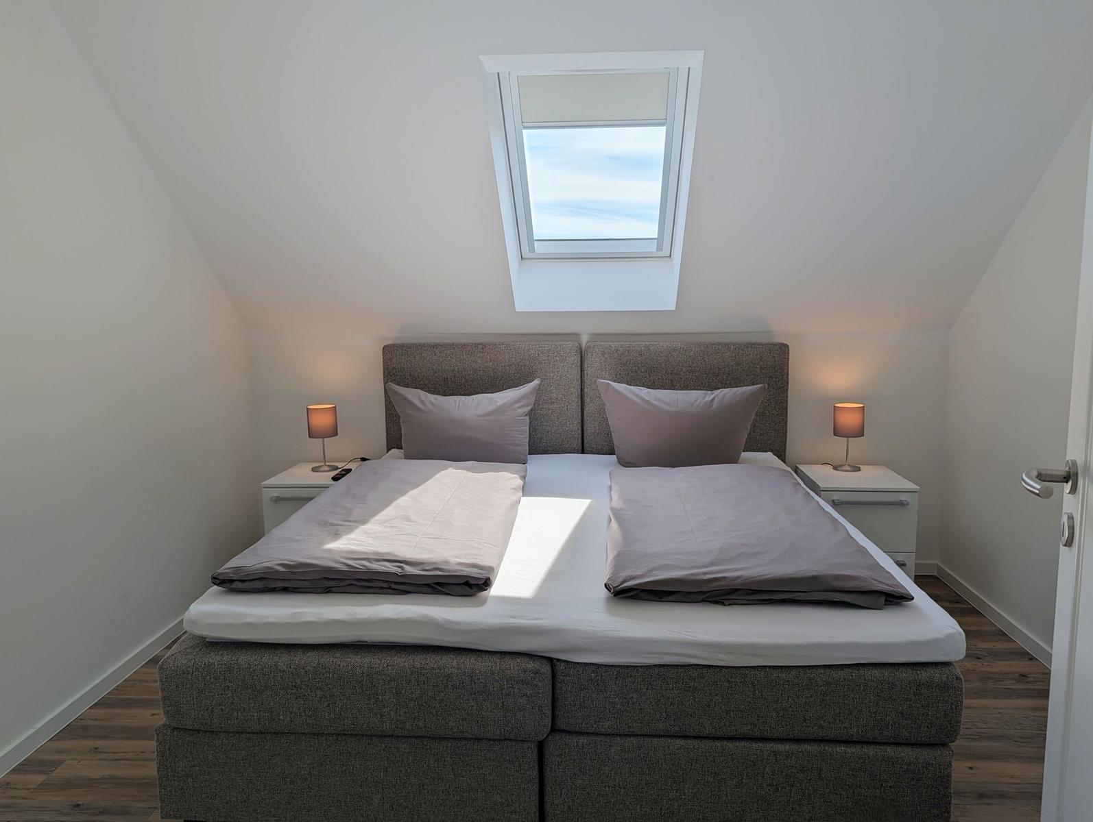Schlafzimmer mit Doppelbett, zwei Nachttischen und Dachfenster.