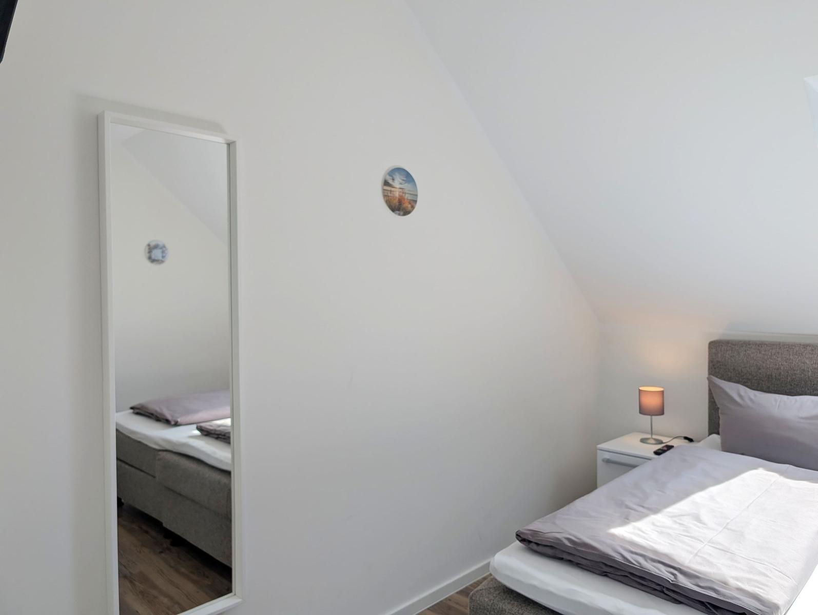 Schlafzimmer mit Bett, Nachttisch und Spiegel an geneigter Wand.