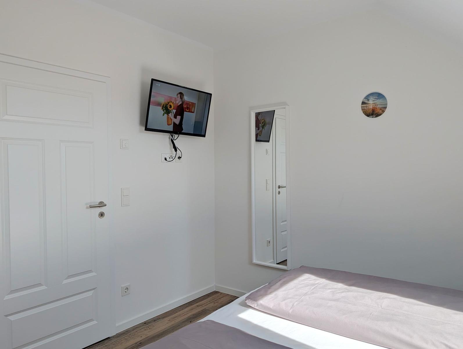 Schlafzimmer mit Bett, Wandfernseher und Spiegel