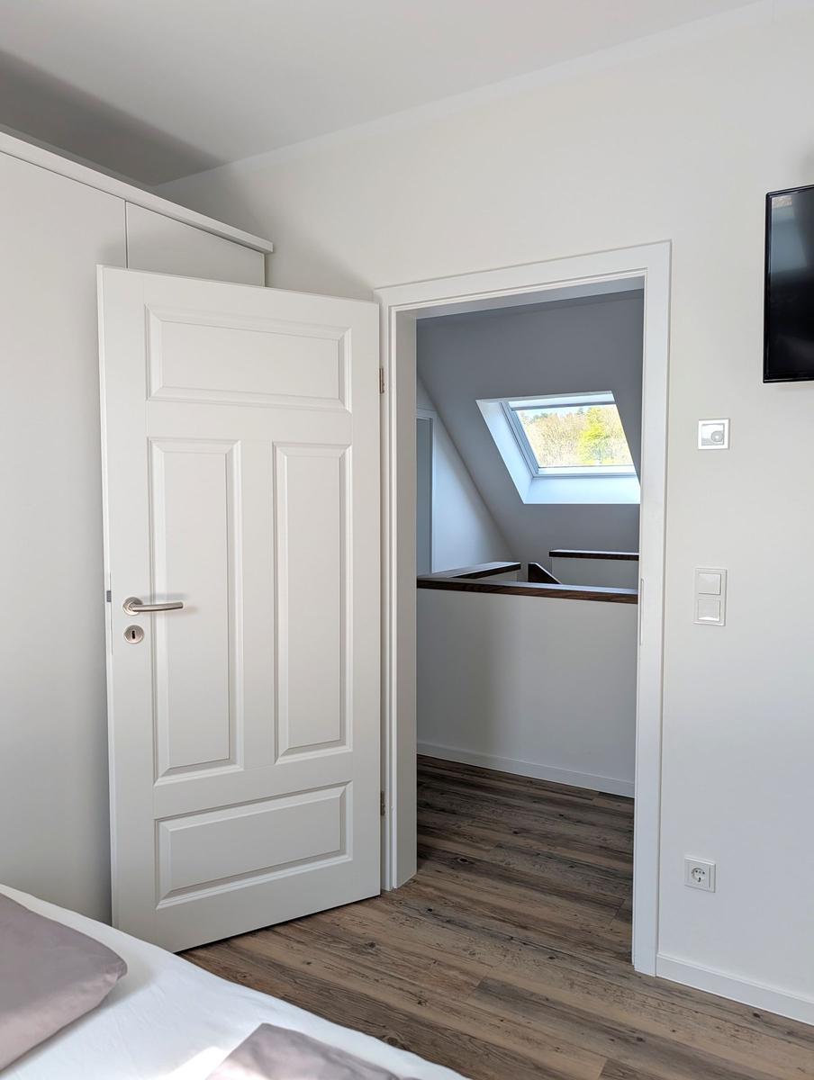 Schlafzimmer mit Tür zu Dachboden, Holzboden und Dachfenster.