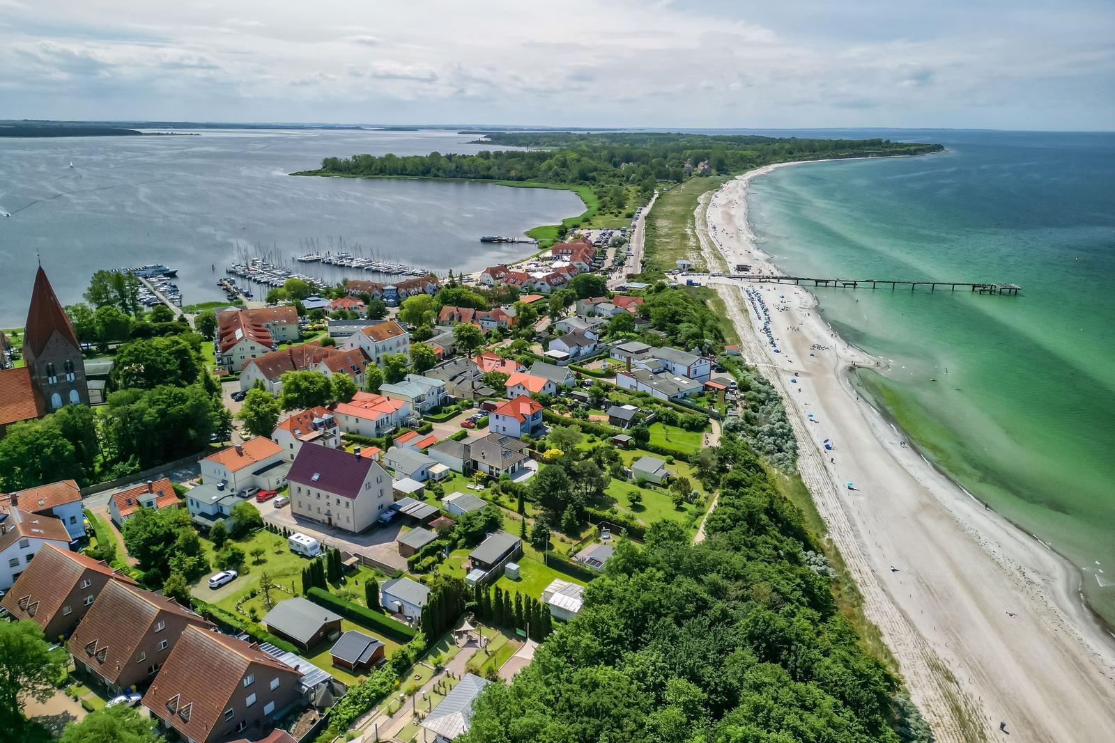 Aussicht auf Küstenort mit Strand, Bootshafen und grünen Gärten.
