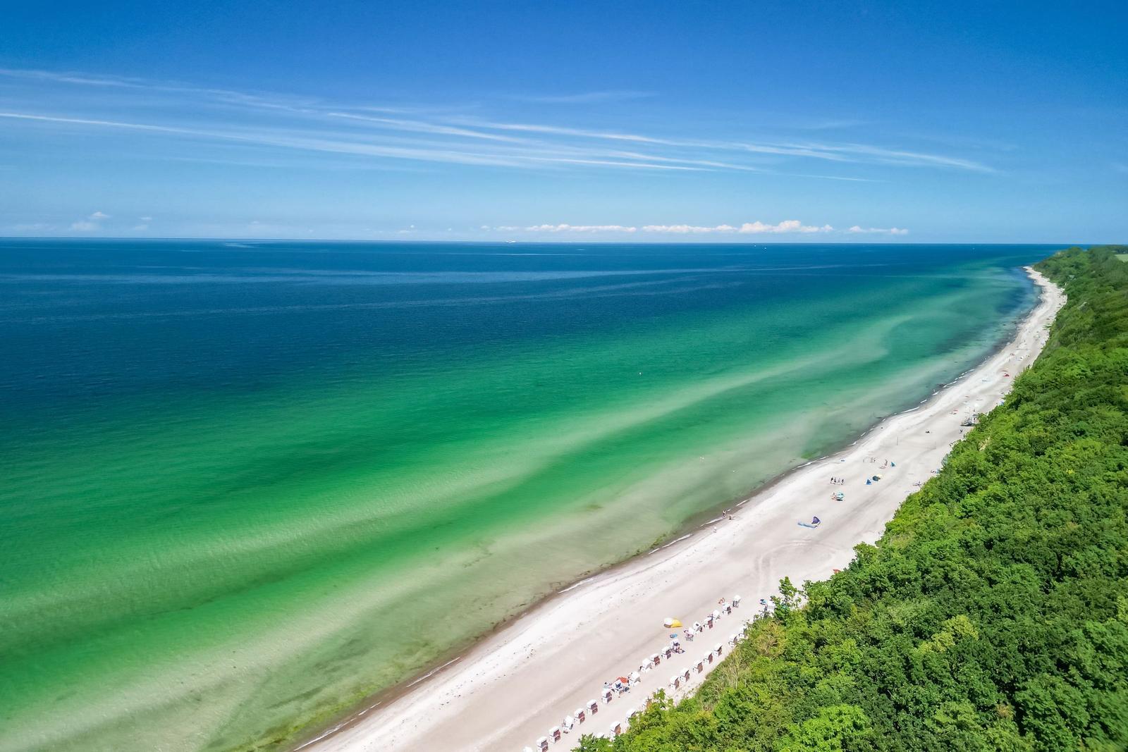 Strand mit klarem Wasser und grüner Vegetation entlang der Küste.
